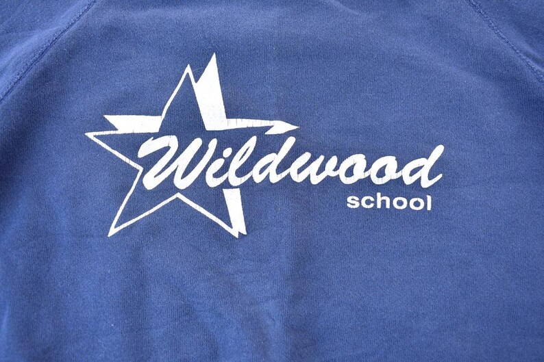 May include: A blue sweatshirt with a white star and the text "Wildwood School" printed on the front.