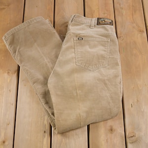 Könnte beinhalten: Eine beige Cordhose mit einem braunen Leder-Patch am hinteren Bund, auf dem "California Classics" steht.