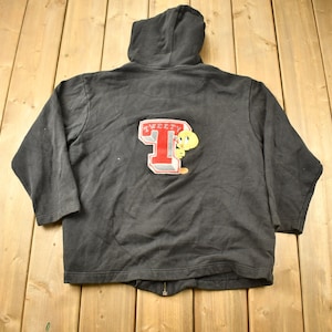 May include: Black zip-up hoodie with a Tweety Bird graphic on the back. The graphic features Tweety Bird peeking out from behind a red and white letter 'T' with the word 'Tweety' above it.