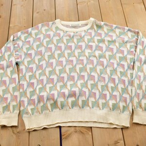 Puede incluir: Un suéter blanco con un patrón geométrico en tonos de rosa, azul y verde.