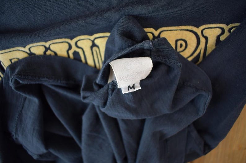 May include: A dark blue t-shirt with a yellow graphic print of the word "DRAGON". The shirt has a white tag with the letter "M" on it.