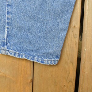 Puede incluir: Primer plano de una pernera de vaqueros azul claro. El dobladillo es visible, mostrando las costuras y el borde de la tela. Los vaqueros est&aacute;n sobre una superficie de madera.