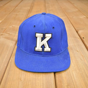 May include: A blue baseball cap with a white felt letter 'K' on the front.