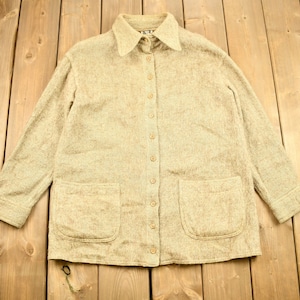 May include: A beige long-sleeved shirt with a button-up front and two patch pockets. The shirt is made of a soft, textured fabric.