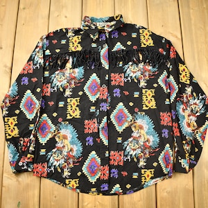 May include: A black long-sleeved shirt with a colourful Native American-inspired pattern. The shirt features a geometric design with fringe along the front.