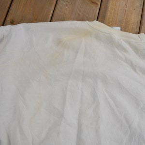 K&ouml;nnte beinhalten: Ein wei&szlig;es Langarmshirt mit einem schwachen gelben Fleck auf dem R&uuml;cken.