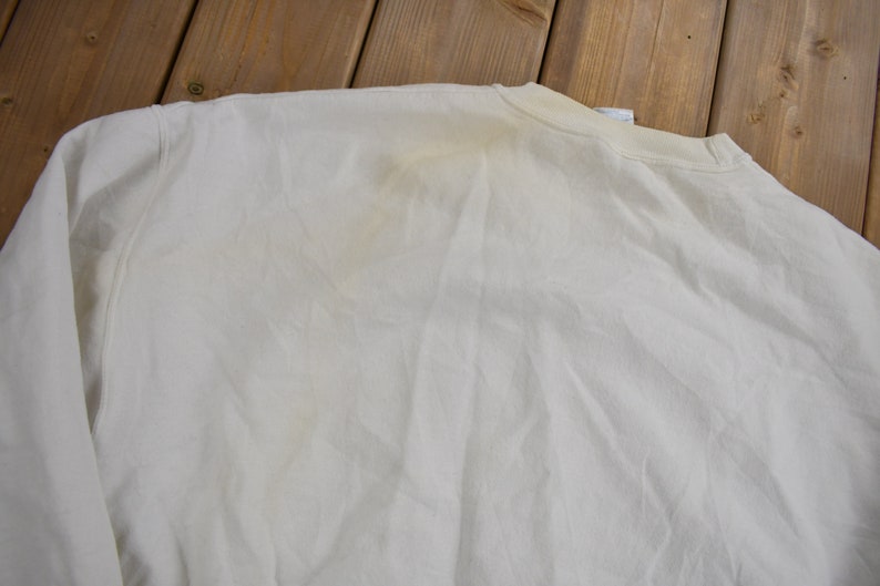 K&ouml;nnte beinhalten: Ein wei&szlig;es Langarmshirt mit einem schwachen gelben Fleck auf dem R&uuml;cken.