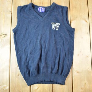May include: Navy blue V-neck sweater vest with a white "W" patch on the chest. The vest has a ribbed hem and a small logo tag at the neckline. The garment is made of a soft, knit fabric.