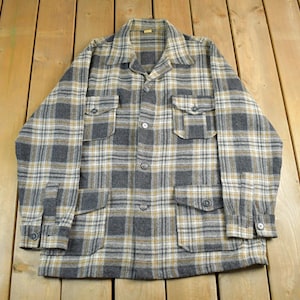 May include: A vintage button-down shirt in a plaid pattern of gray, tan, and white. The shirt has a collared neckline, two chest pockets, and two lower pockets. The long-sleeved shirt is made of a thick, woven fabric.