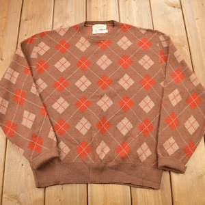 May include: A brown sweater with a red and beige argyle pattern.