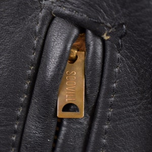 May include: Close-up of a black leather jacket zipper with a gold Scovill zipper pull.