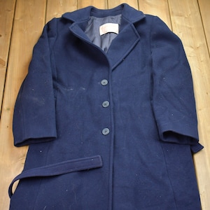 Pu&ograve; includere: Un cappotto di lana blu navy con cintura e quattro bottoni. Il cappotto ha uno stile classico e sartoriale.