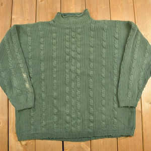 May include: A dark green cable knit sweater with a mock neck. The sweater has a distressed look with some fraying around the edges.