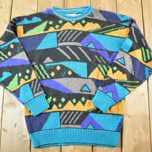 May include: A vintage crew neck sweater with a geometric pattern. The sweater features a mix of colors including black, teal, yellow, purple, and gray. The cuffs and hem are teal, and the collar has a thin yellow stripe.