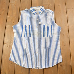 May include: A sleeveless button-down shirt with blue and white vertical stripes. The shirt has two chest pockets and a collar.