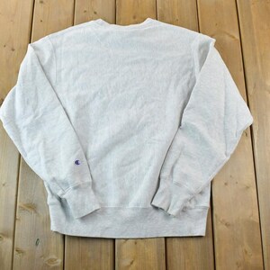 Puede incluir: Una sudadera gris Champion con un peque&ntilde;o logotipo en la manga izquierda.