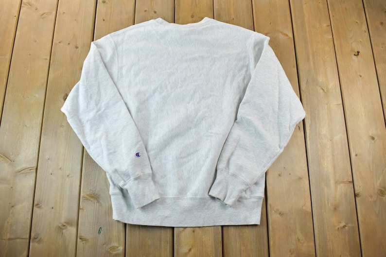 Puede incluir: Una sudadera gris Champion con un peque&ntilde;o logotipo en la manga izquierda.