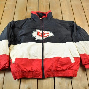 May include: A black, white, and red jacket with a Kansas City Chiefs logo on the front. The jacket is a full-zip style with a drawstring waist.