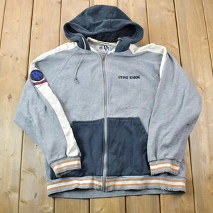 May include: A grey and blue zip-up hoodie with a white stripe down each sleeve. The hoodie has a hood with a drawstring and a logo on the left sleeve. The text "PEPSI EHM" is embroidered on the front of the hoodie.