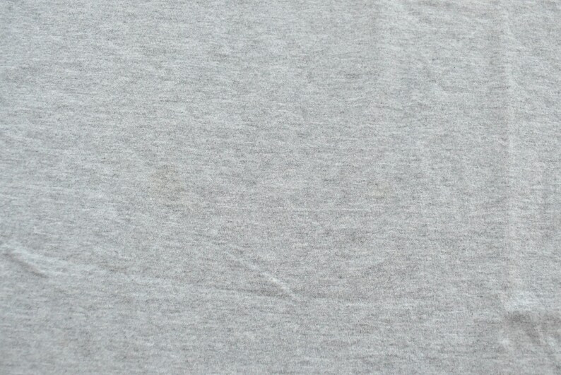 Puede incluir: Primer plano de una tela gris claro con una superficie texturizada. La tela parece ser un material de punto o jersey, con sutiles variaciones de color y textura. La imagen muestra los detalles del textil.