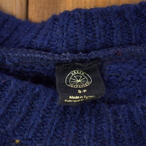 May include: A navy blue sweater with a yellow and white pattern. The sweater has a tag that says "Urban Outfitters" and "S-P" with the text "Made in Turkey" below.