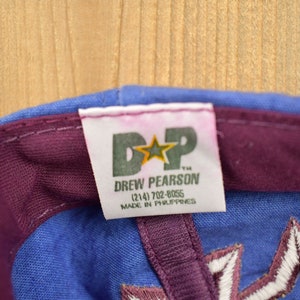 May include: A blue and purple baseball cap with a white star and the text "D*P Drew Pearson (214) 702-8055 Made in Philippines" on a white tag.