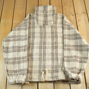 May include: A vintage, beige and brown plaid pullover sweater with a high collar. The sweater has long sleeves and a drawstring at the waist. The fabric appears to be a thick, woven material.