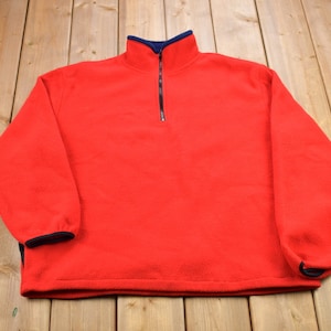 May include: A red fleece pullover with a half-zip closure and navy blue trim around the collar, cuffs, and hem.