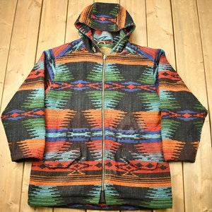Puede incluir: Una chaqueta con capucha con un patrón geométrico colorido en tonos de rojo, naranja, azul, verde y negro. La chaqueta tiene una cremallera y dos bolsillos.