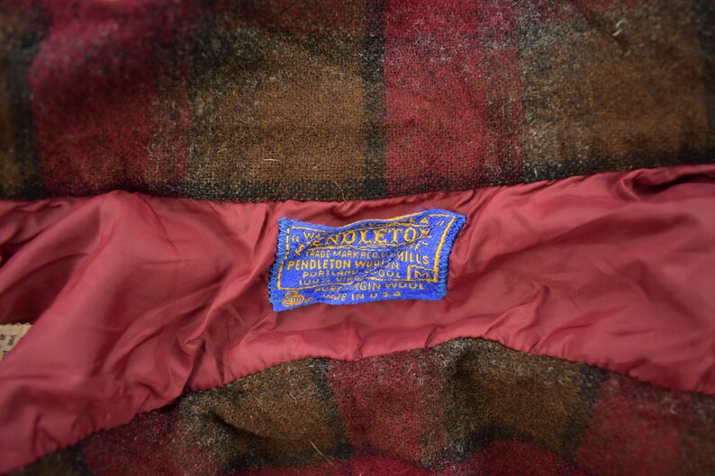 May include: A blue label with white text that reads "The Woolmark, Trade Mark, Pendleton Woolen Mills, Portland, Oregon, 100% Virgin Wool, Made in U.S.A."