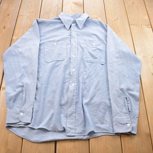 May include: A light blue long-sleeved button-down shirt with two chest pockets.