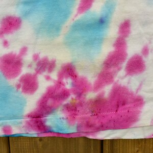 May include: A white t-shirt with a tie-dye pattern in shades of pink and blue.