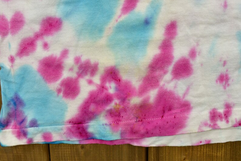 May include: A white t-shirt with a tie-dye pattern in shades of pink and blue.