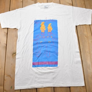 May include: White t-shirt featuring a blue and pink graphic print of two figures with yellow flames for hair. The text "Limited Edition" is printed below the figures.