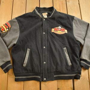 May include: Black and grey varsity jacket with a Mickey Mouse logo and the text "M&M's" on the front. The sleeves are grey with a black stripe at the cuffs. The jacket has a snap closure.