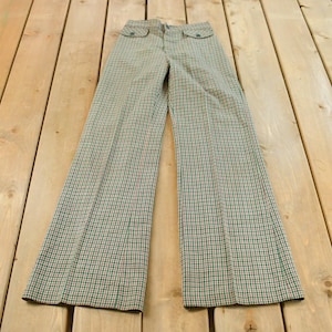 May include: A pair of vintage, wide-leg pants with a plaid pattern in green, red, and white. The pants have two front pockets and a button closure. The pants are laid flat on a wooden surface.