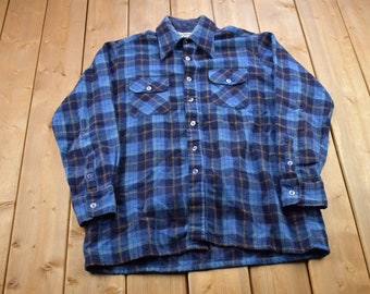 Può includere: Una camicia di flanella a quadri blu e marroni con maniche lunghe e due tasche sul petto.