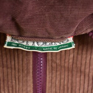 May include: A brown corduroy jacket with a zipper closure and a green and white label that reads "BOITOLLINO MADE BY JAPAN RN 81157".