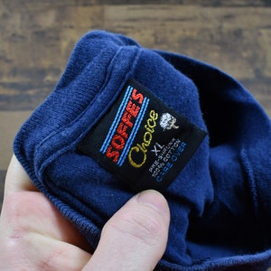 May include: A blue t-shirt with a black tag that reads "SOFFES Choice" and "XL" in white text. The tag also says "Pre-Shrunk 100% Cotton Care Over"