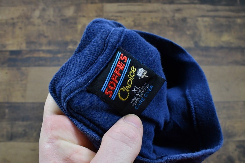 May include: A blue t-shirt with a black tag that reads "SOFFES Choice" and "XL" in white text. The tag also says "Pre-Shrunk 100% Cotton Care Over"