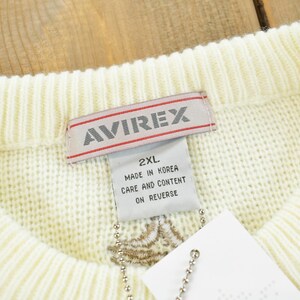 May include: Cream-colored sweater with a ribbed collar. The label reads "AVIREX" in red and white. A tag attached to the sweater displays "2XL" and "Made in Korea". The sweater has a textured knit design.