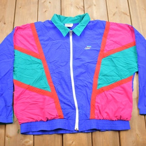 May include: A blue, pink, green and red windbreaker jacket with a zip fastening and a logo on the left chest. The jacket has a geometric pattern.