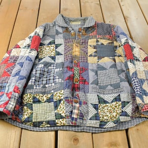 May include: A long-sleeve button-down jacket constructed from a patchwork quilt featuring various fabric squares in red, blue, yellow, and white. The garment displays a repeating star pattern across the front and sleeves with a collar.