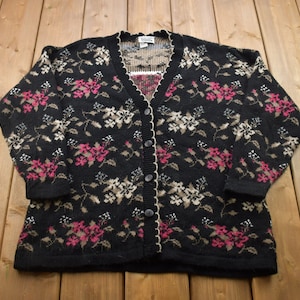 May include: Black cardigan sweater with a floral pattern in pink, white, and brown. The cardigan has a button closure and a scalloped trim.