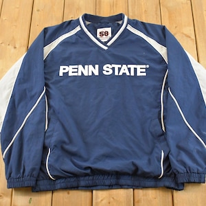 Puede incluir: Chaqueta tipo jersey azul marino de Penn State con detalles en blanco y el texto "PENN STATE" en el pecho. La chaqueta tiene cuello en V y un diseño blanco y gris en las mangas.