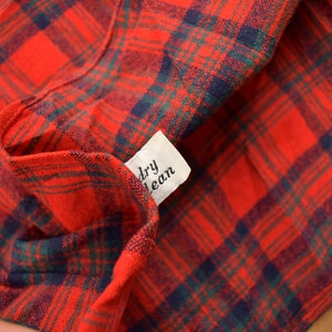 Puede incluir: Primer plano de una tela de cuadros rojos y verdes con una etiqueta blanca que dice "limpieza en seco".