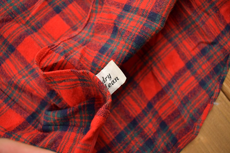 Puede incluir: Primer plano de una tela de cuadros rojos y verdes con una etiqueta blanca que dice "limpieza en seco".