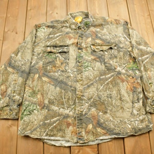 May include: A long-sleeved button-up shirt with a camouflage pattern in shades of brown, green, and white.