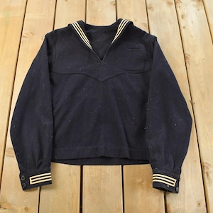 Peut inclure: Chemise de marin bleu marine avec col en V et manches longues. Le col et les poignets présentent des rayures jaunes. La chemise est faite d'un tissu épais et foncé et a un style classique et vintage.