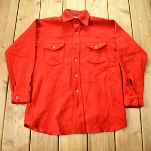 May include: A red long-sleeved flannel shirt with a button-up front and two chest pockets.